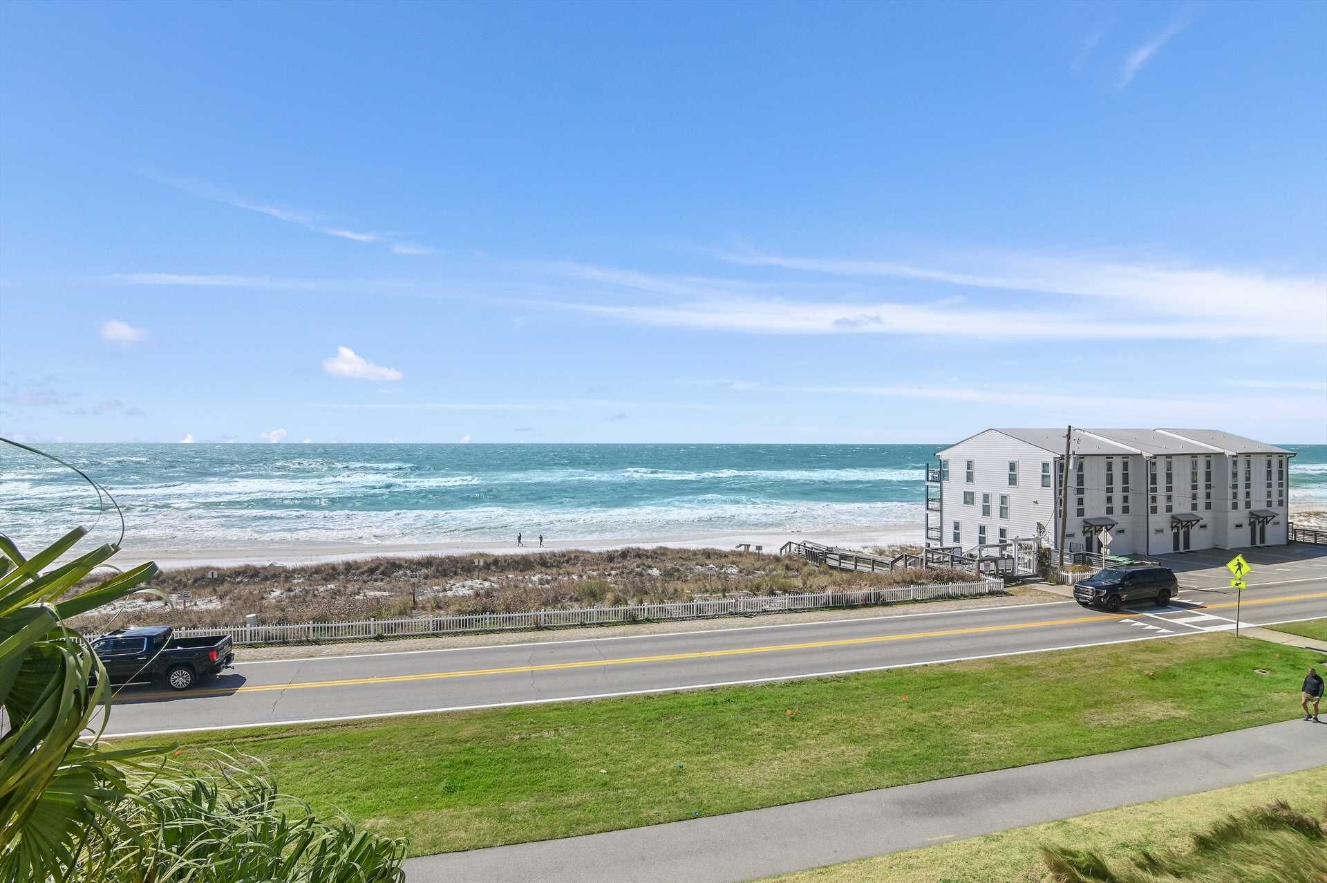 Une route côtière avec vue sur la plage, un immeuble à plusieurs étages et un ciel dégagé.