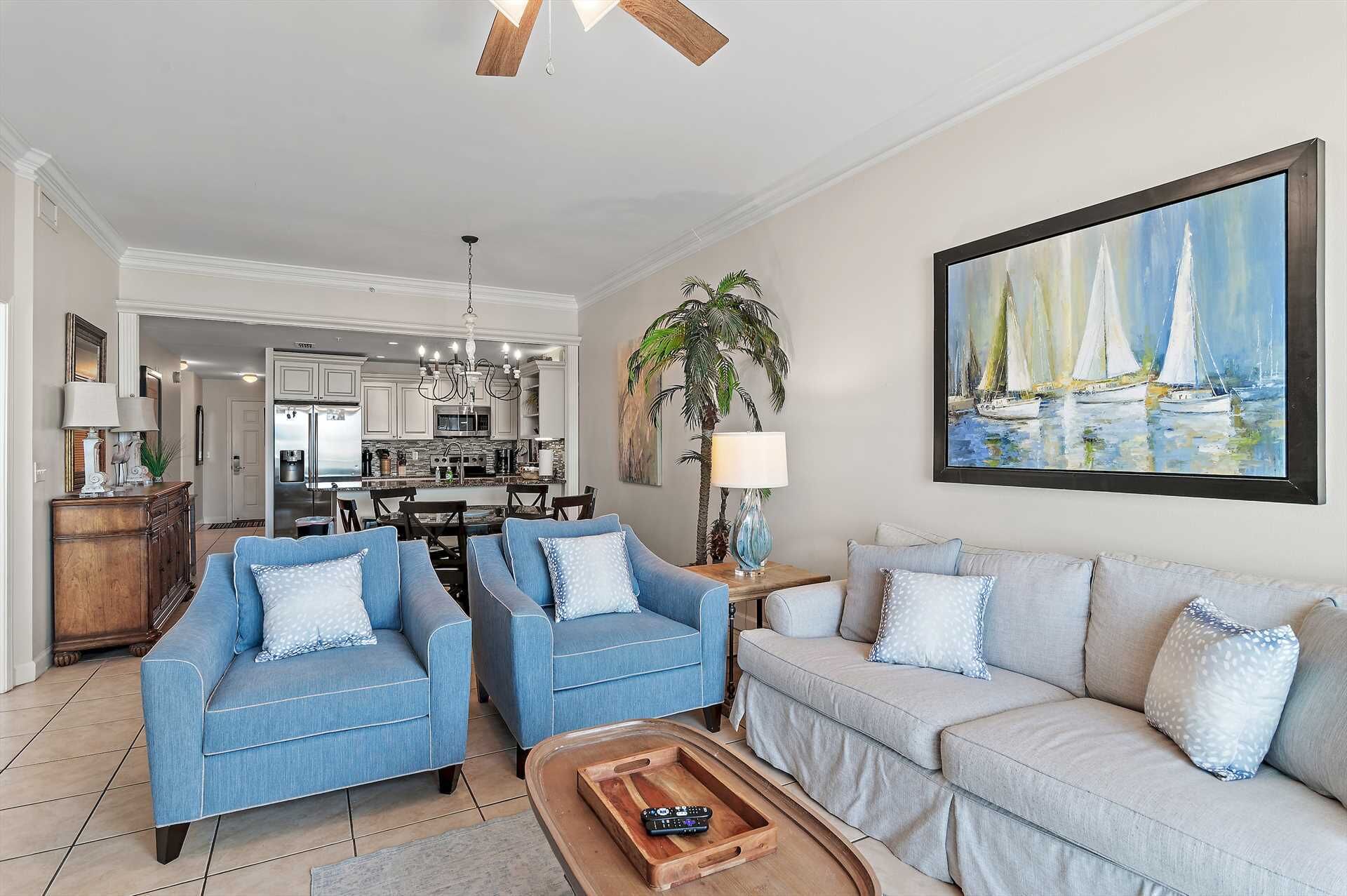 A living room with two blue sofas, a grey sofa, a wooden coffee table, and a painting of sailboats.