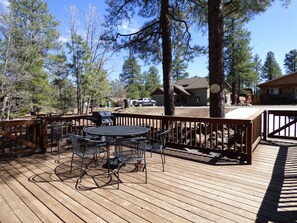 A wooden deck with outdoor furniture, surrounded by trees and a house in the background.