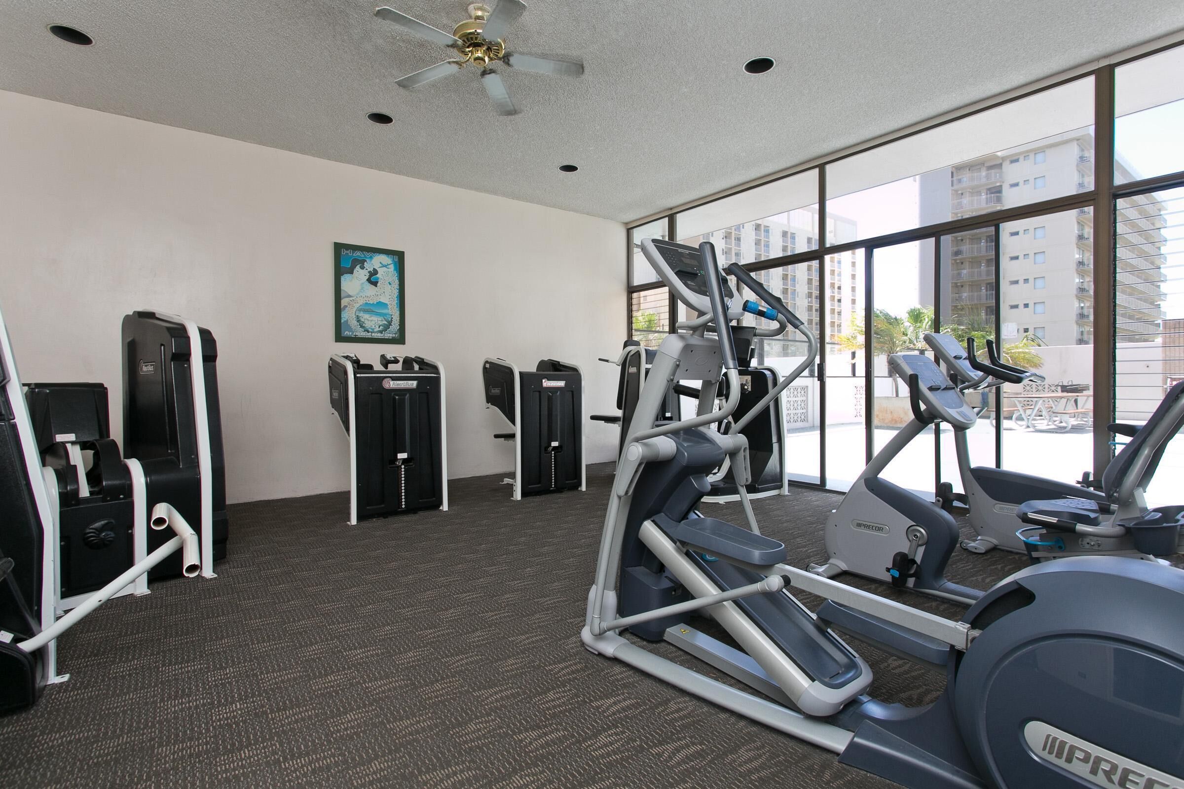 Een fitnessruimte met cardioapparatuur, krachttrainingsapparatuur en een groot raam met uitzicht over de stad.