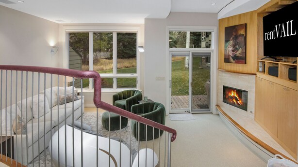 A modern living room with a staircase, a fireplace, and a large window overlooking a garden. - Coldstream Townhome 38 | Stylish 3BR Cascade Village Retreat (Vail)