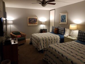 A hotel room with two beds, a chair, a desk, a TV, and artwork on the walls.