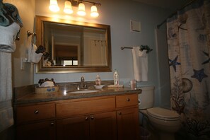A bathroom with a wooden vanity, a sink, a mirror, a toilet, and a shower curtain with a nautical theme.