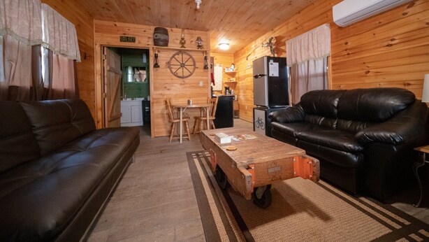 A cozy cabin interior with a wooden interior, a black leather sofa, a wooden coffee table, and a kitchenette area.