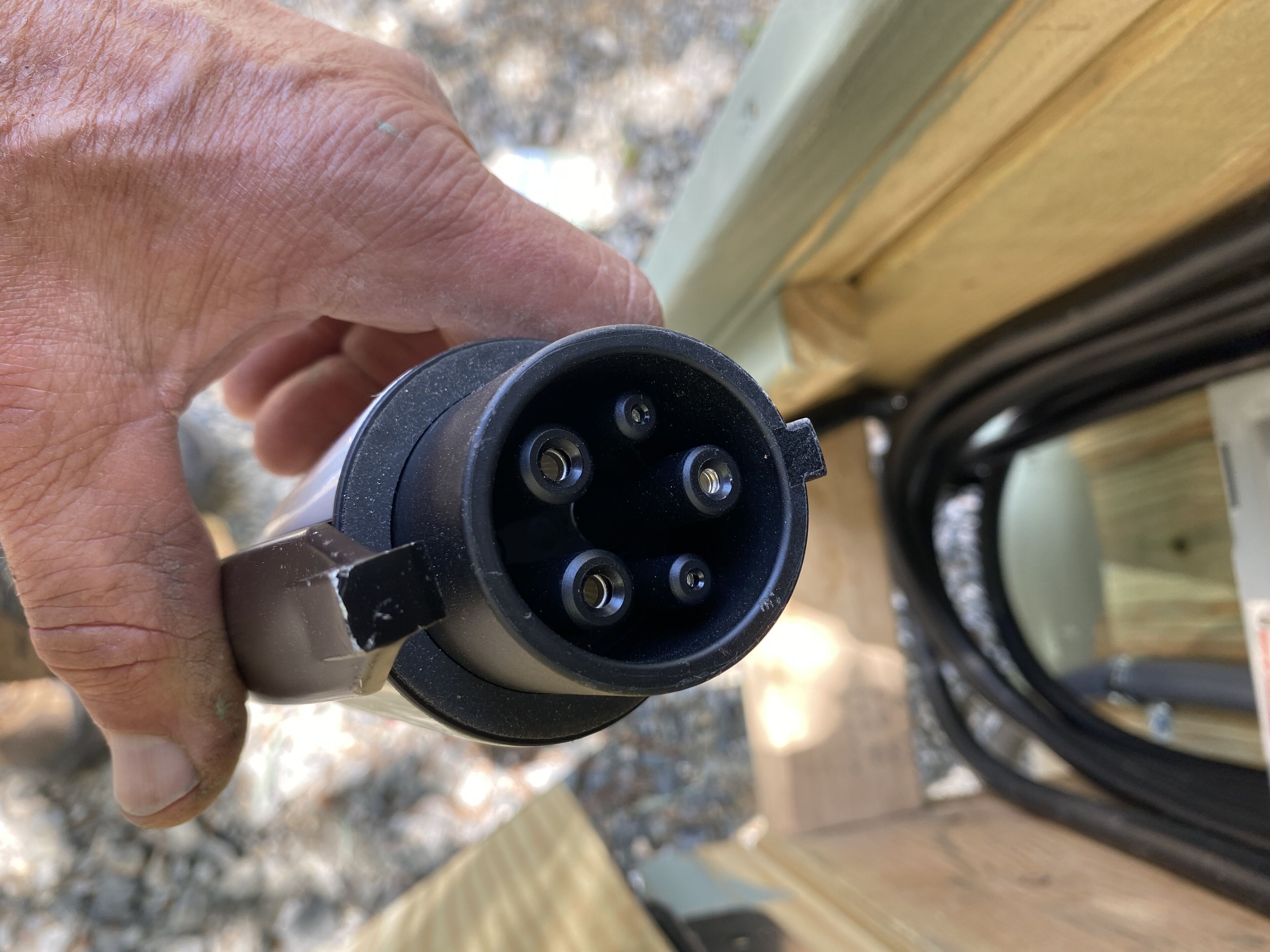 A close-up of a hand holding a car charger with four prongs, inserted into a car's charging port.