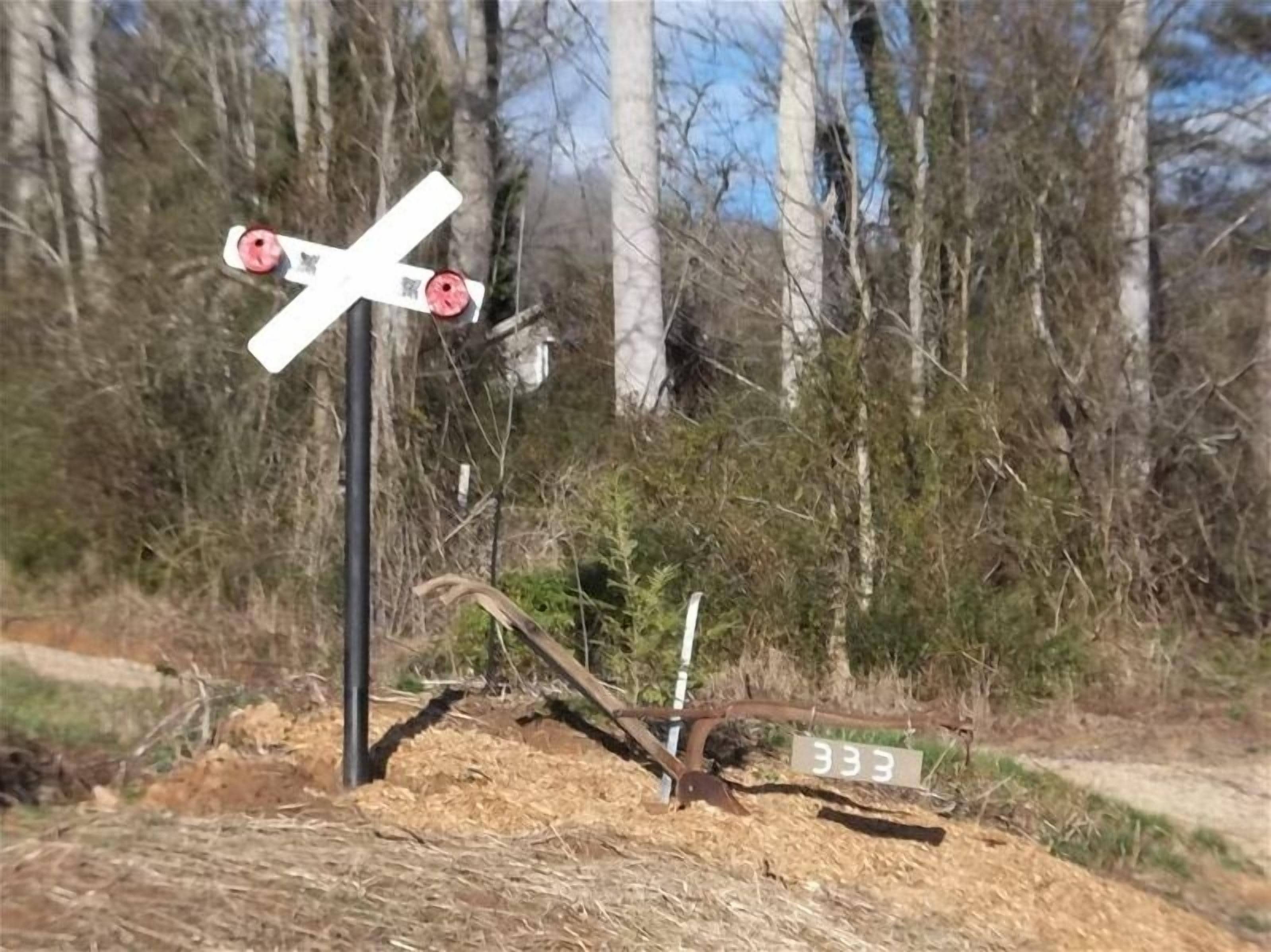 A railroad crossing sign with a number plate labeled '333' in a wooded area.