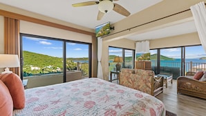 A hotel room with a large bed, a balcony with a view of the sea, and a television on the wall.