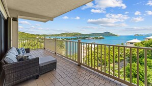 A balcony with a wicker sofa and a view of a coastal landscape.