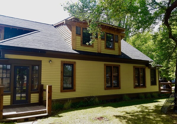 Ein gelbes, zweistöckiges Haus mit dunklem Dach, einer Holzveranda und zahlreichen Fenstern.