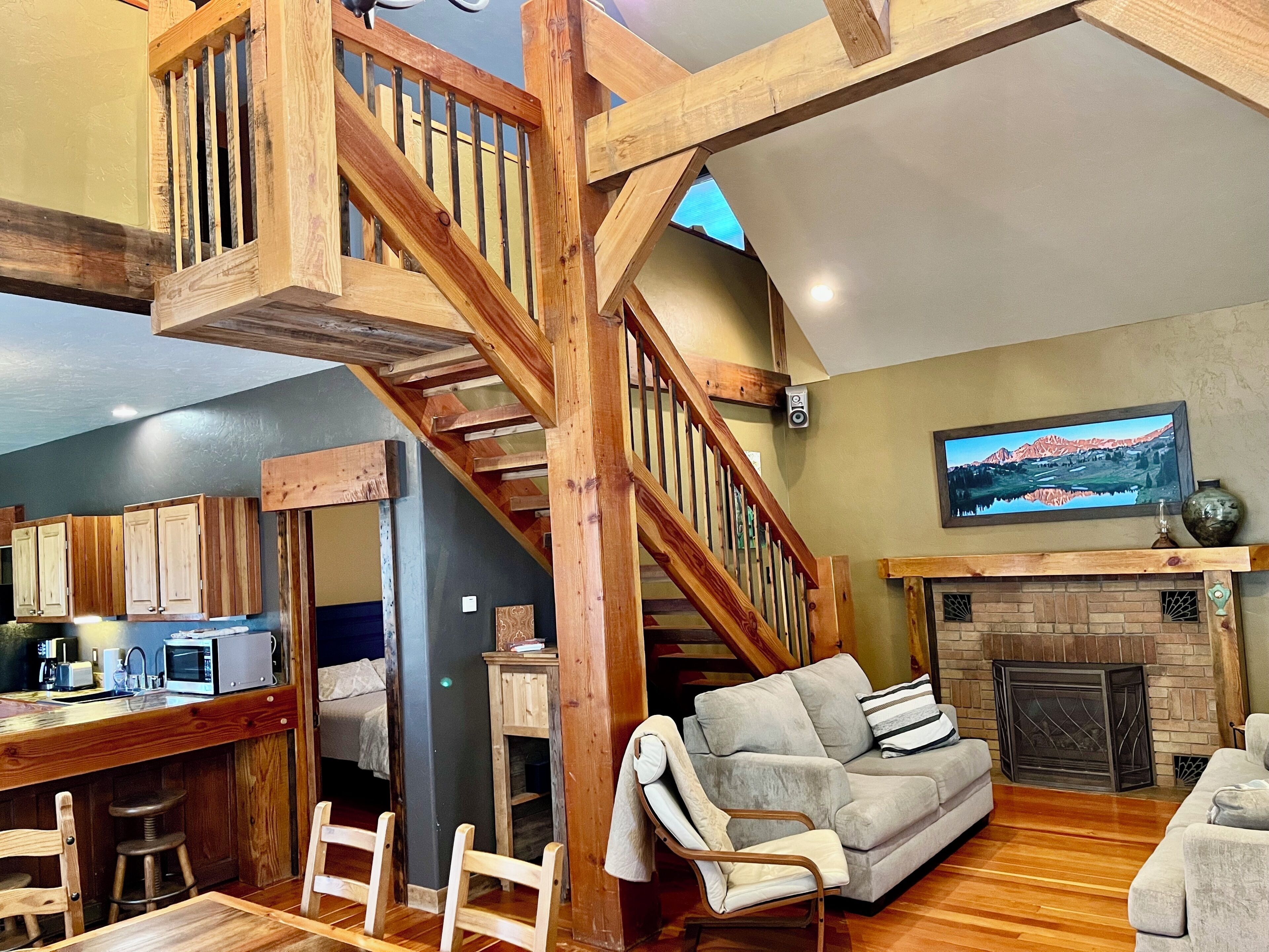 Un vaste espace de vie agrémenté d’un escalier en bois, d’une cheminée, d’un téléviseur fixé au mur et d’un coin cuisine équipé d’appareils électroménagers modernes.
