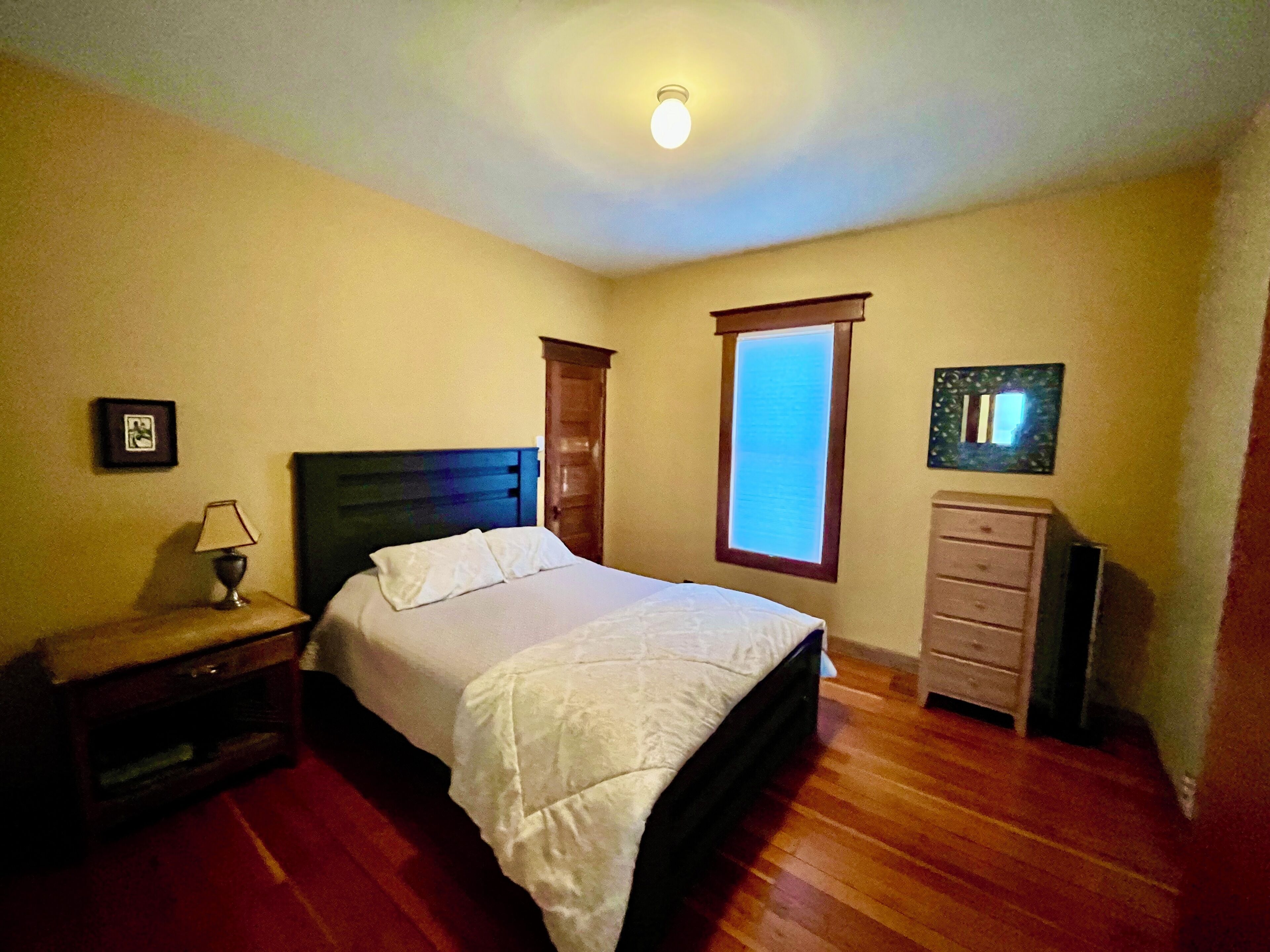 Een slaapkamer met een bed, nachtkastje, kaptafel en raam.