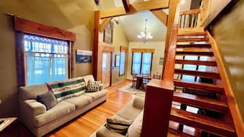 A spacious living area with a wooden staircase, a sofa set, and a dining table.