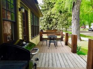 Eine Holzterrasse mit Grill, Sitzgelegenheit und Blick auf eine Straße.