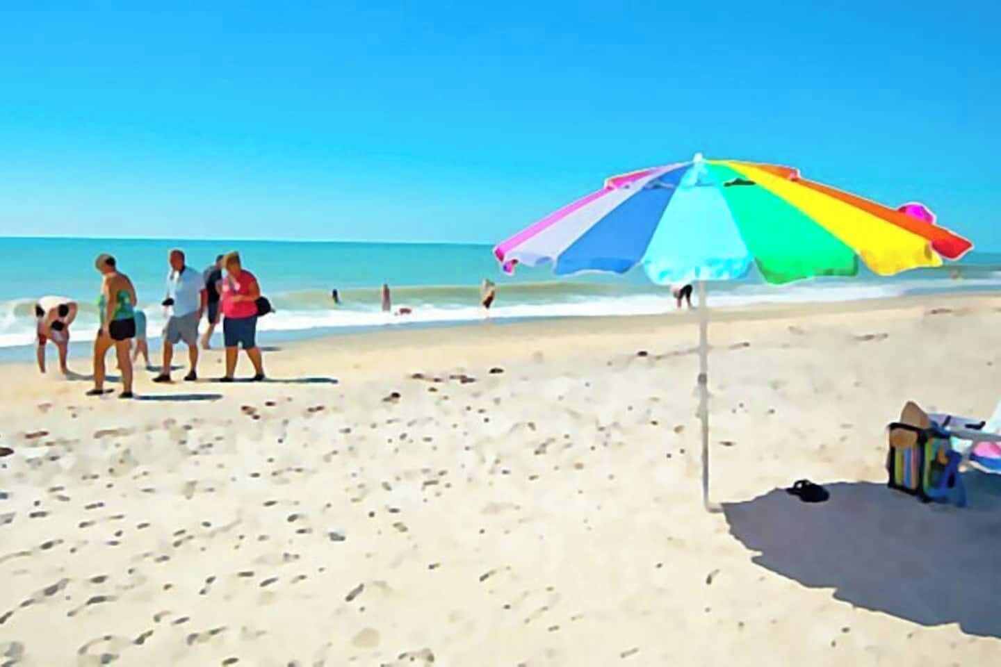 A beach scene with a colorful umbrella, people walking, and a clear sky.