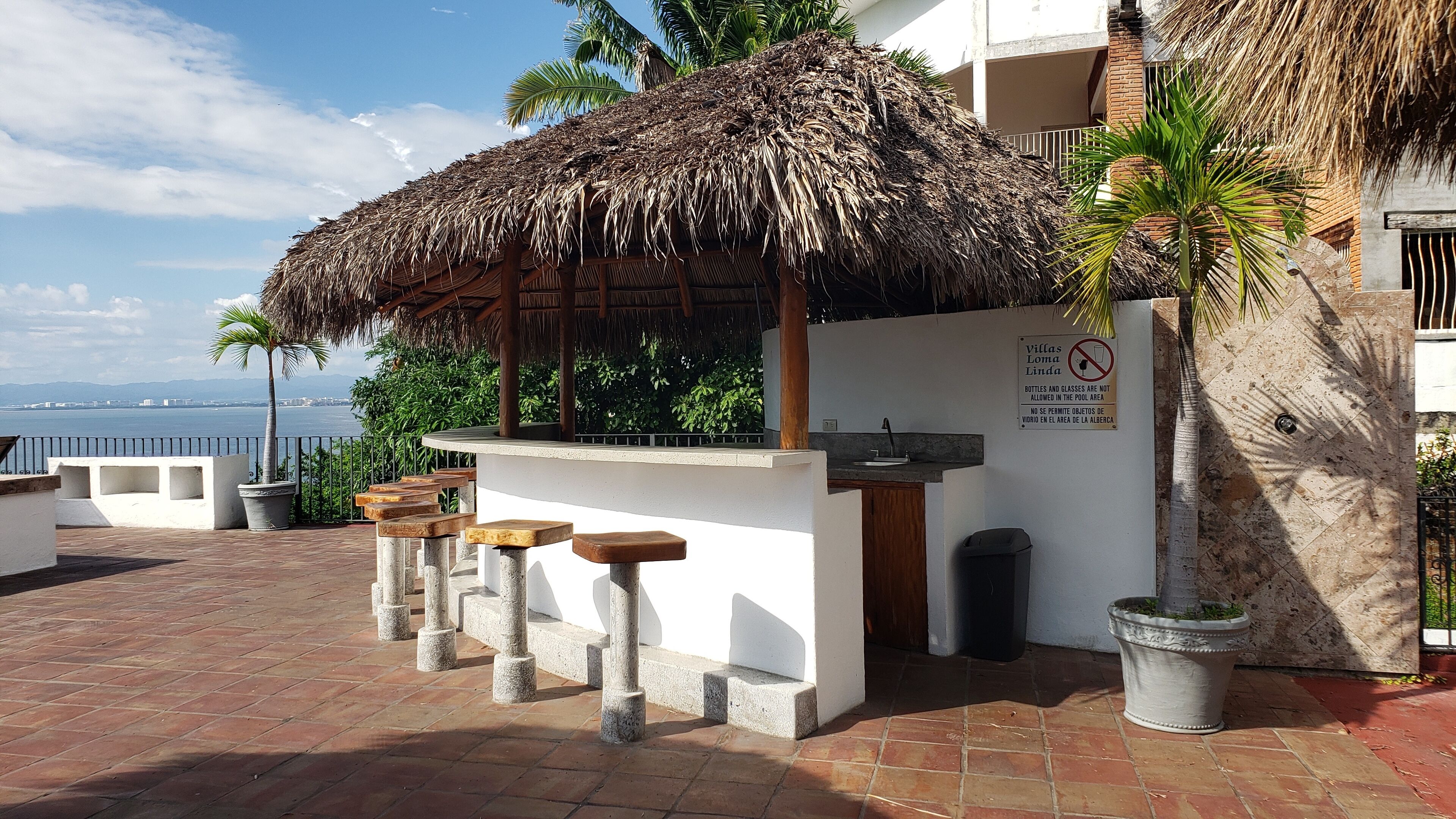 Una terraza con techo de paja, mobiliario exterior, zona junto a la piscina y vista al mar.