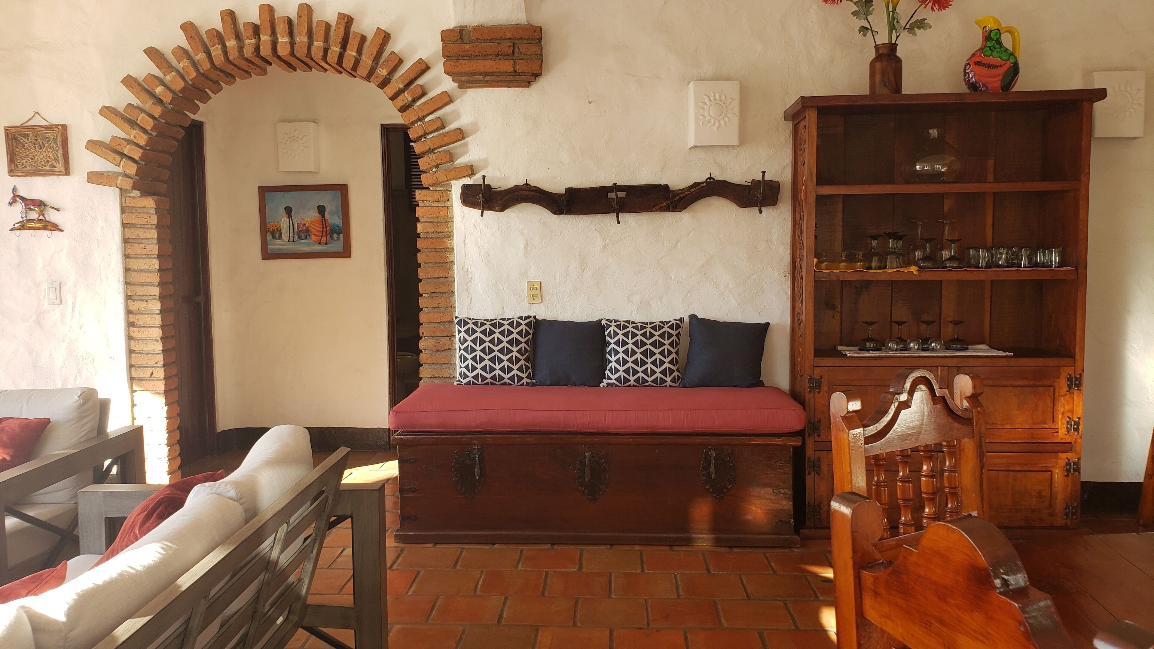 Ein gemütliches Wohnzimmer mit einer Holzbank, einem roten Sofa und einem Holzschrank mit Gläsern.