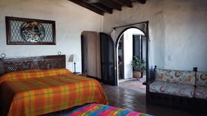 Un dormitorio con una cama grande, un sofá, una planta en maceta y un ventanal con vidrieras.