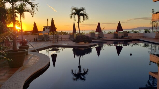 Una piscina con vista al atardecer, sillas de descanso y palmeras.