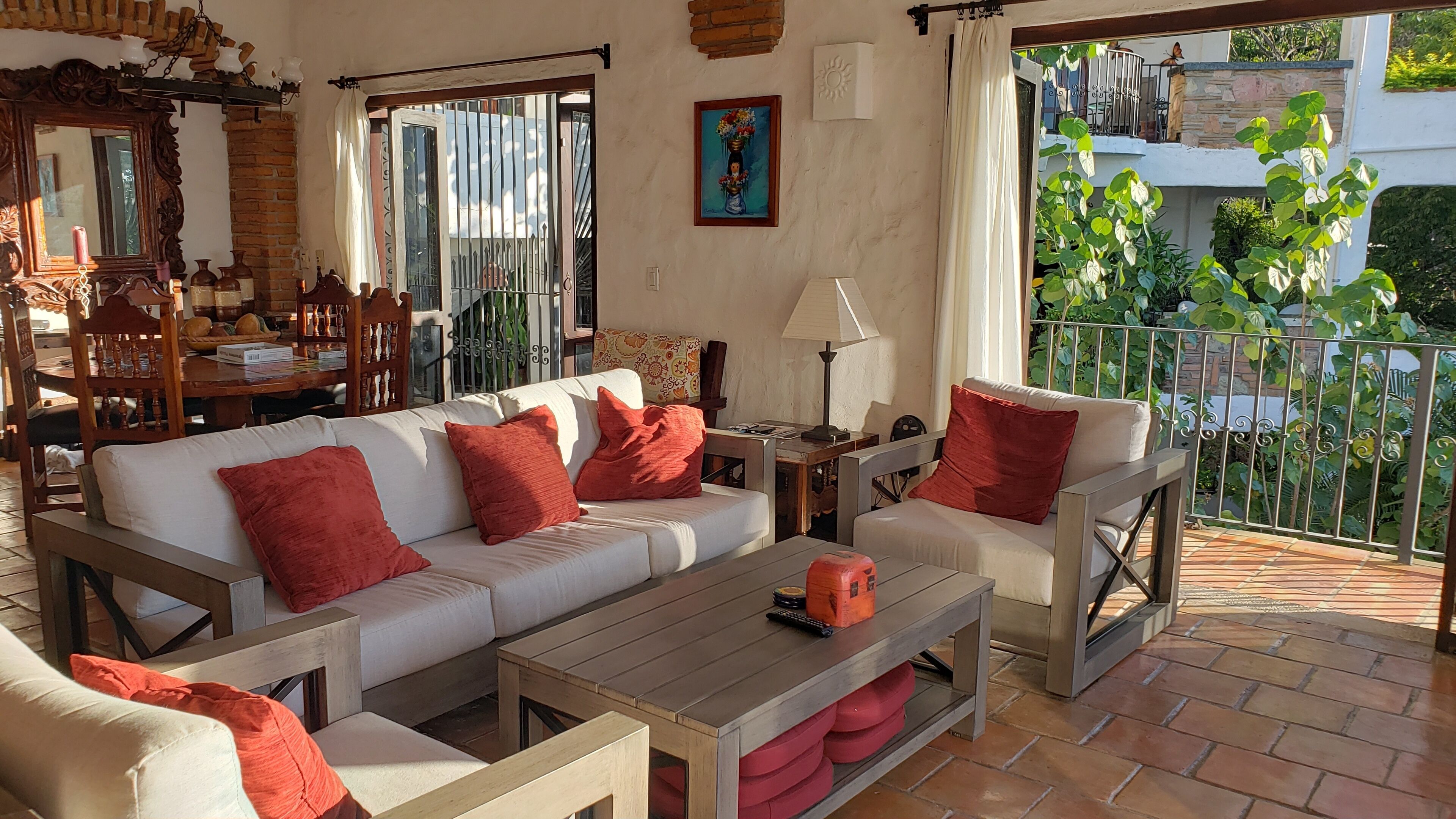 Un salón acogedor con sofá, sillones y una mesa de centro. Hay una zona de comedor con mesa y sillas, y un balcón con plantas.
