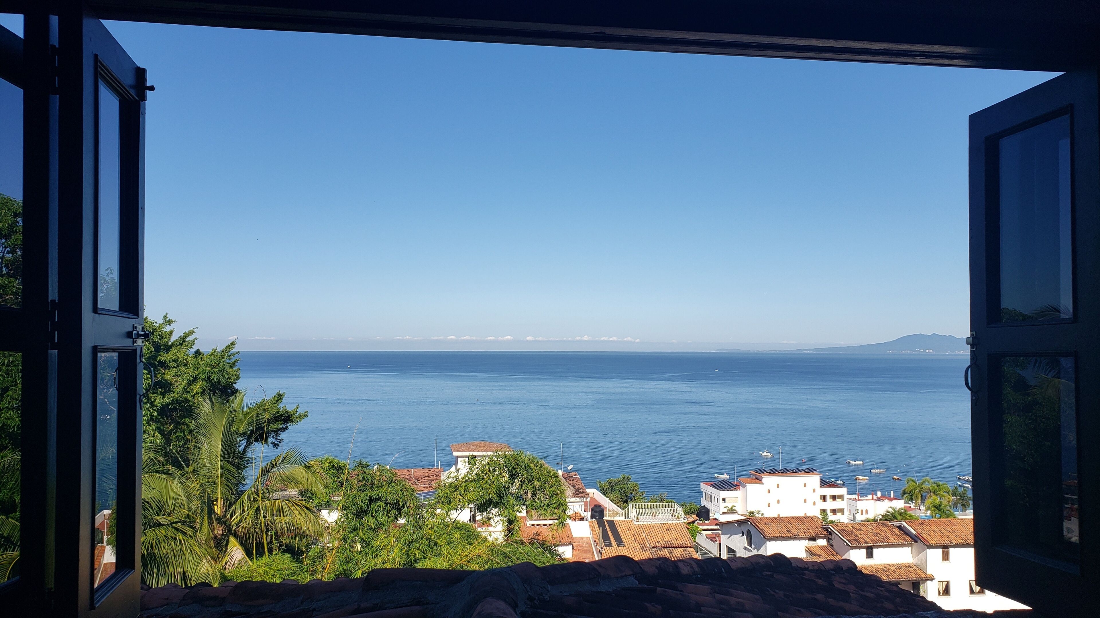Une vue sur la côte, prise depuis une fenêtre donnant sur une mer calme, avec des bâtiments et de la végétation au premier plan.