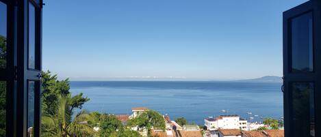 Une vue sur la côte, prise depuis une fenêtre donnant sur une mer calme, avec des bâtiments et de la végétation au premier plan.
