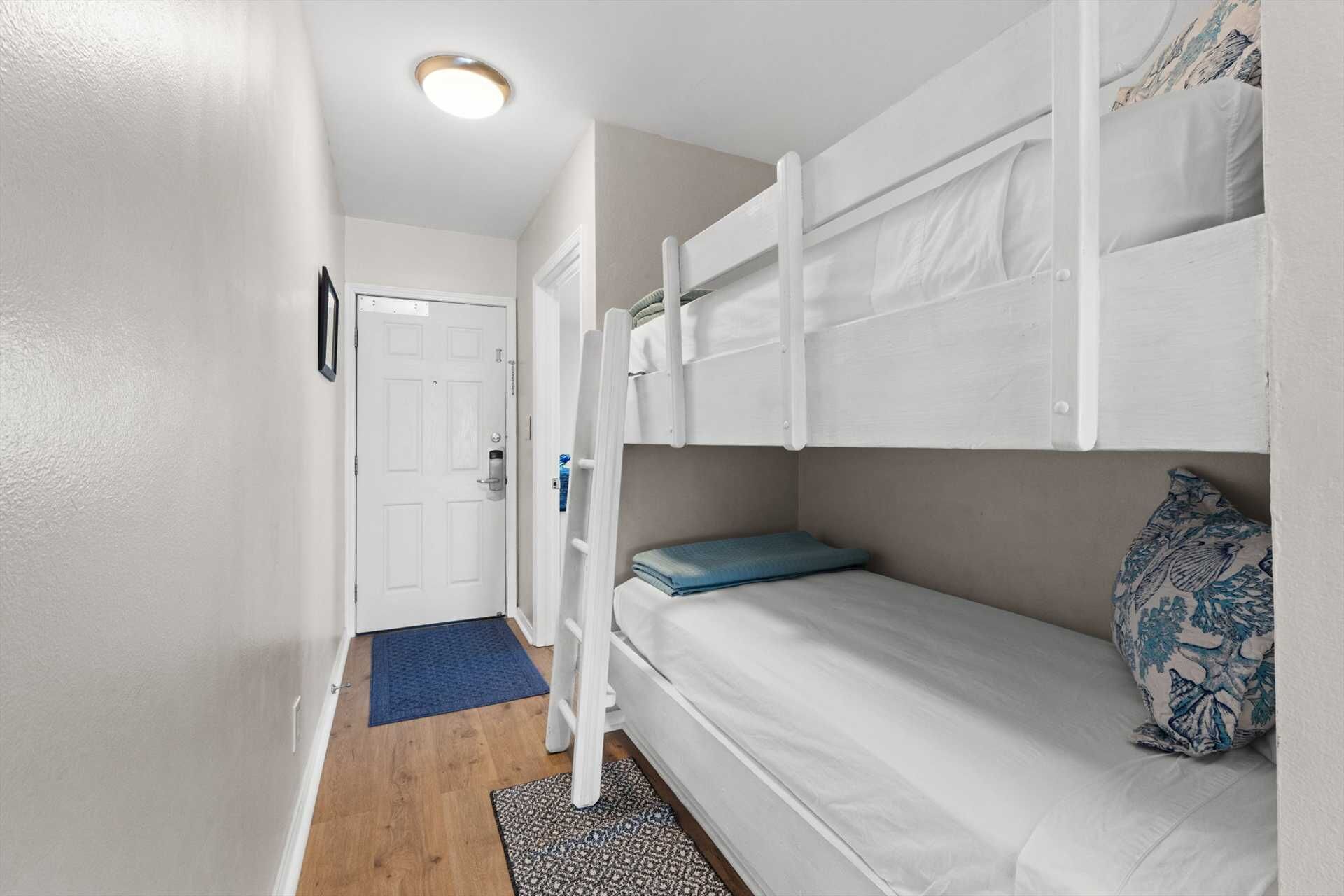 A compact room with bunk beds, a door, and a small rug.
