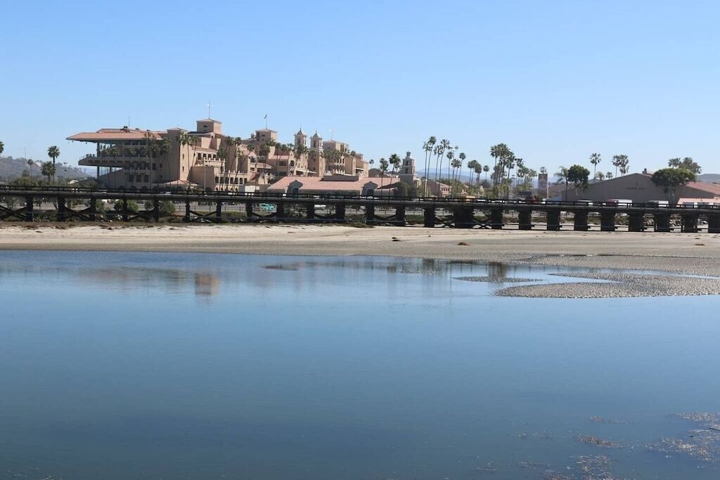 Een hotel aan de kust met een groot gebouw, palmbomen en een brug over stil water.