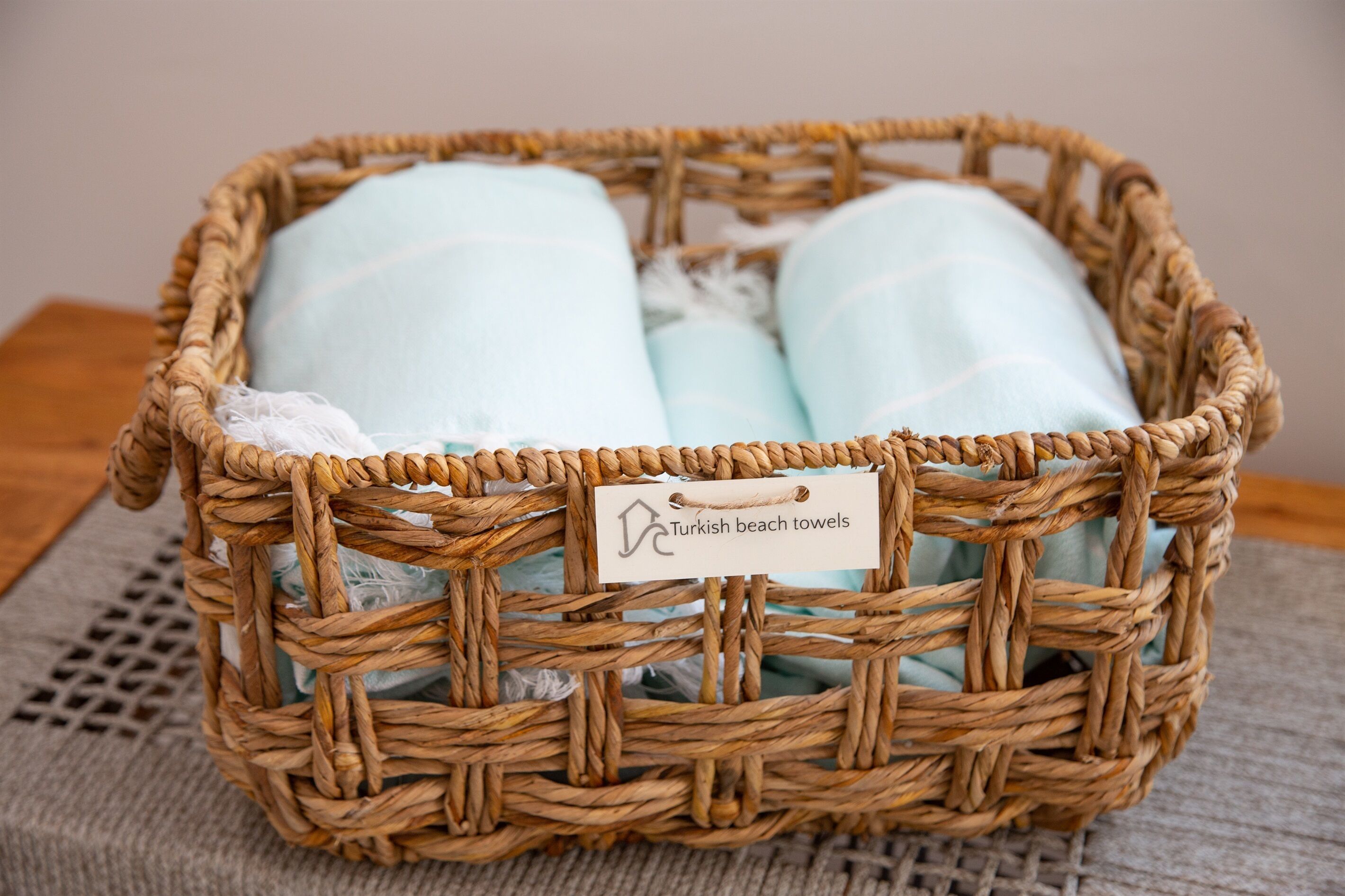 A wicker basket containing light blue towels labeled "Turkish beach towels."