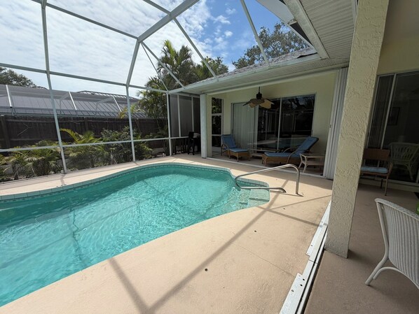 Une piscine entourée de parois en verre, des chaises longues et un ventilateur de plafond.