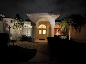 A well-lit entrance with a covered porch, a door, and a pathway leading to the main building. - TOP Rated Premium Costal Family Retreat with Heated Pool & Private Golden Beach (Venice)