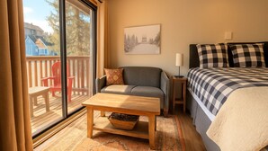 Et værelse med seng, sofa, bord og et vindue med udsigt til en terrasse.