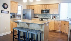 Une cuisine moderne avec des meubles en bois, un réfrigérateur en acier inoxydable, un four à micro-ondes et un grand îlot central doté de tabourets de bar.
