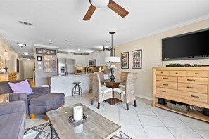 A modern living room with a sofa, coffee table, and a dining area with wicker chairs and a glass table.