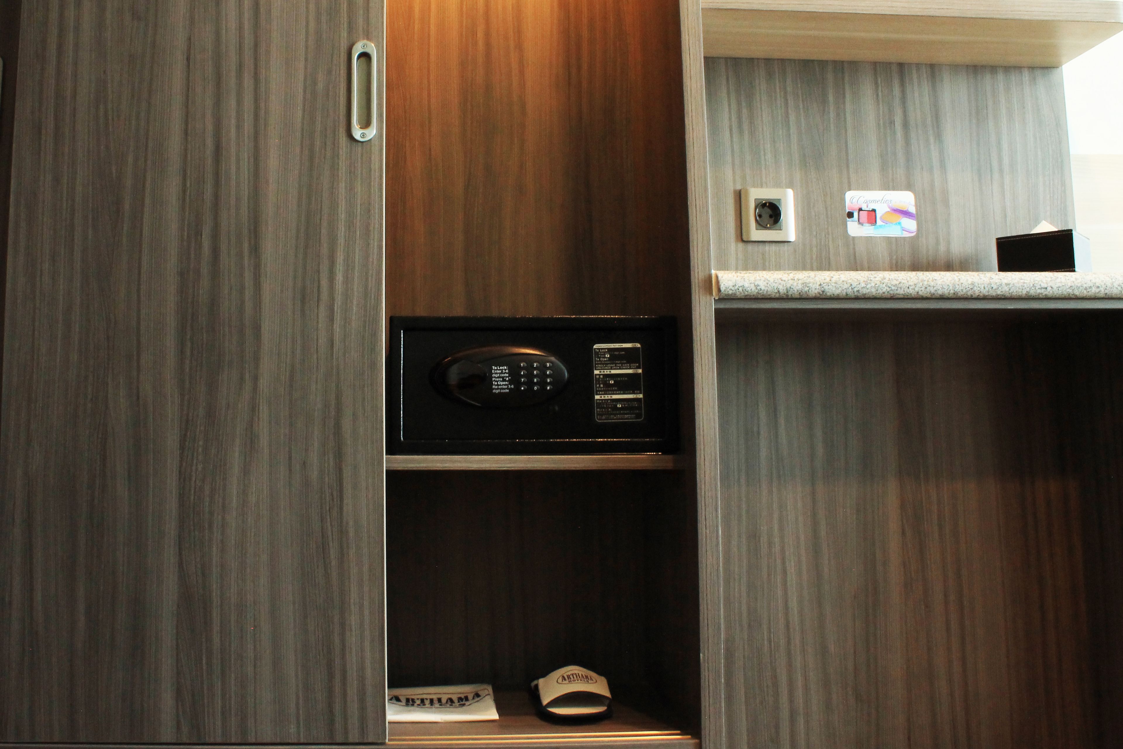 A wooden cabinet with a microwave on the lower shelf and a small shelf above it with a power outlet and a picture frame.