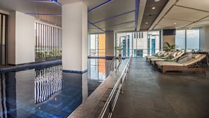 An indoor swimming pool with lounge chairs and a view of the city.