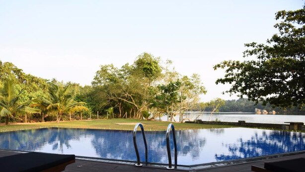 Ein Swimmingpool mit zwei Liegestühlen auf einer Holzterrasse, umgeben von Bäumen und Blick auf einen See.
