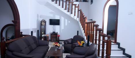 A living room with a staircase, a sofa, a coffee table, and a TV.