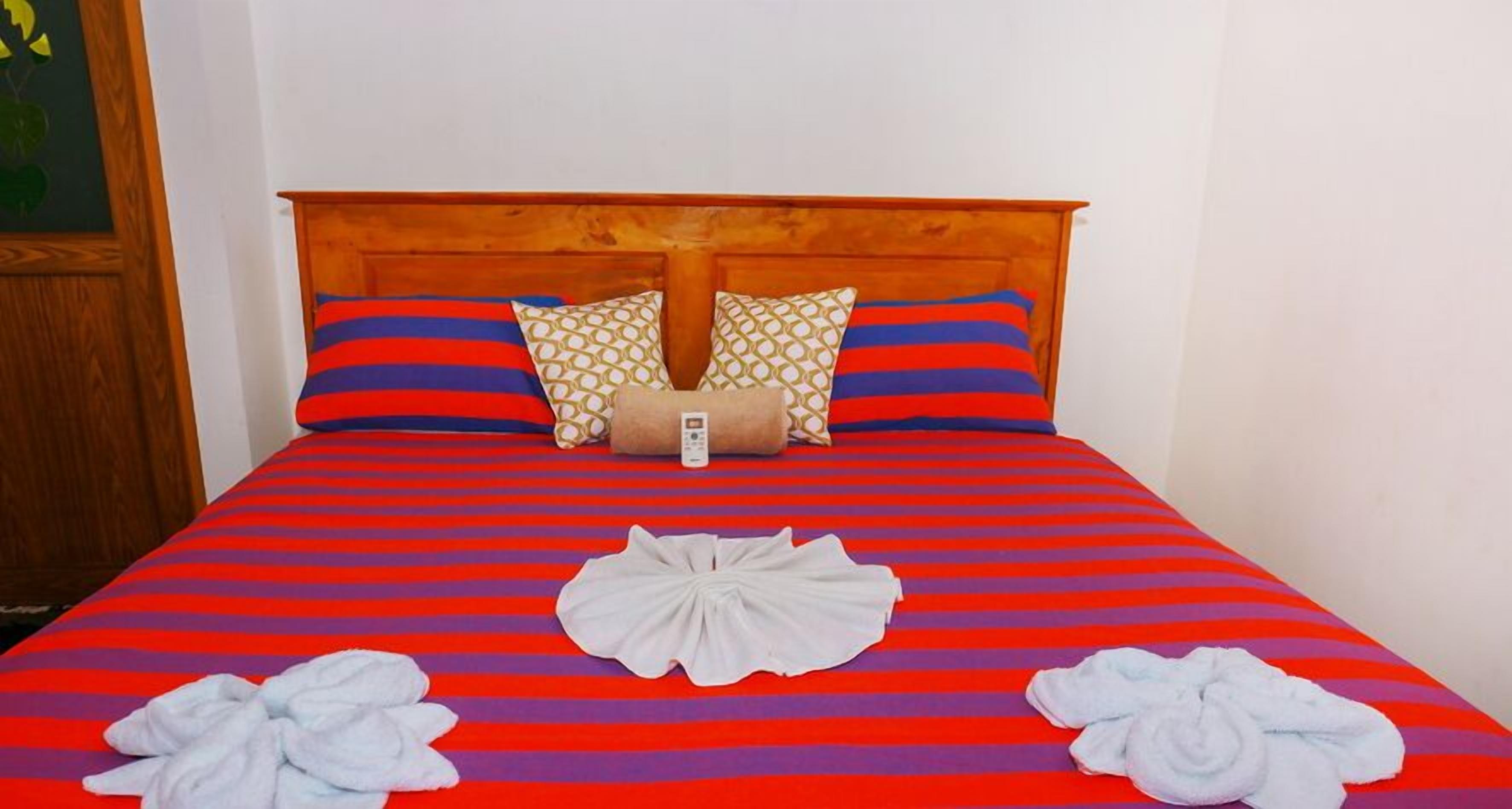 Ein Bett mit einer rot-blauen Streifenauflage, zwei Kissen mit einem geometrischen Muster und zwei weiße Handtücher darauf.