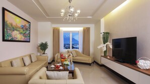 A living room with a sofa, a coffee table with fruits and candles, a TV, a painting, and a view of a mountain through a window. - Sunrise Hotel (Tan Ninh)