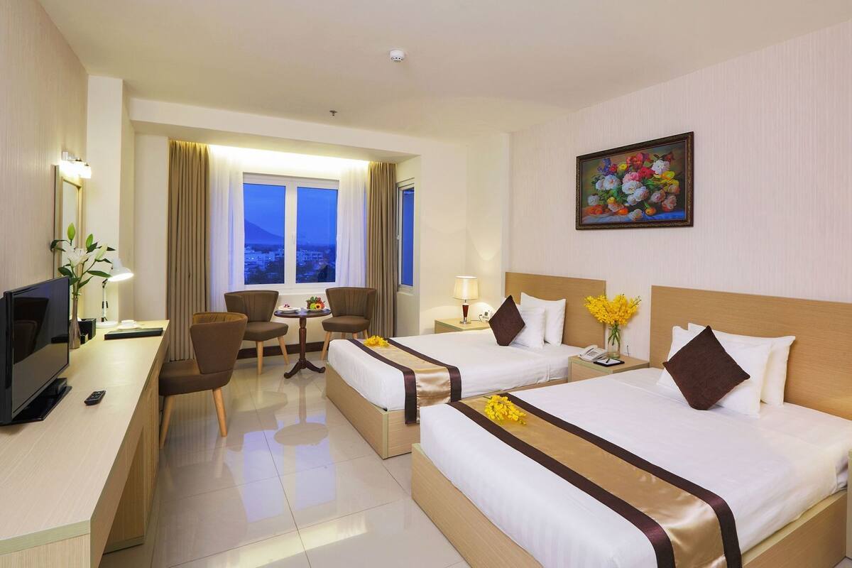 A hotel room with two beds, a desk, a TV, and a painting on the wall.