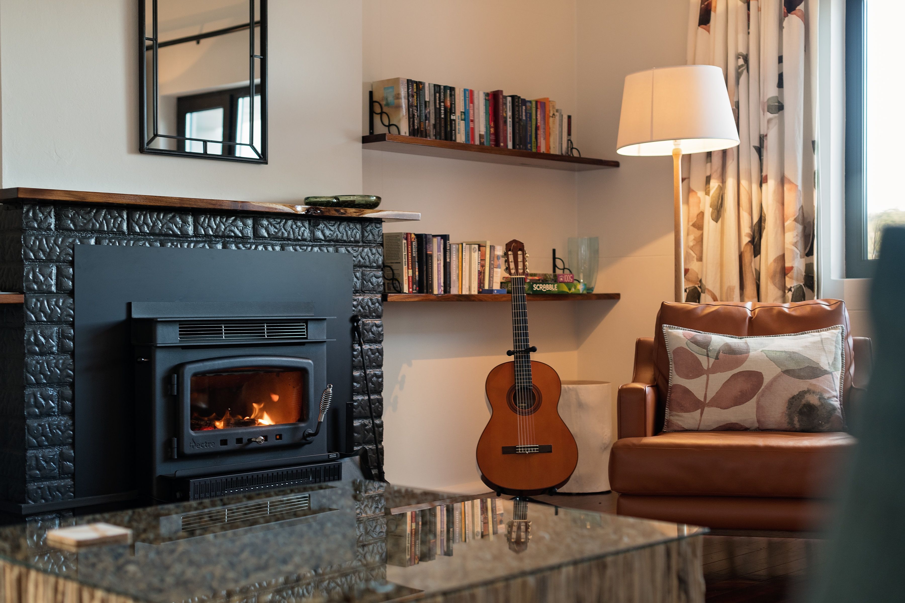 A cozy living room with a fireplace, a bookshelf, a guitar, and a comfortable sofa.