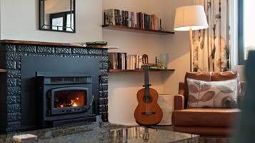 A cozy living room with a fireplace, a bookshelf, a guitar, and a comfortable sofa.