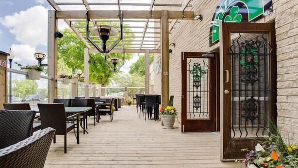 An outdoor patio area with wooden flooring, wicker furniture, and potted plants. - West Wing at Park Town (Saskatoon)
