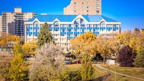 A modern building with a blue roof and large windows, surrounded by autumn trees and a parking area. - West Wing at Park Town (Saskatoon)
