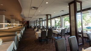 A spacious restaurant with a long counter, multiple tables, and chairs. - West Wing at Park Town (Saskatoon)