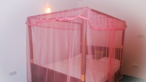 A single bed with a pink mosquito net in a room with white walls and a green floor. - Talalla Sea Anemone Hotel (Talalla)