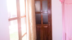 A room with a wooden door, a window with a curtain, and a mat on the floor. - Talalla Sea Anemone Hotel (Talalla)