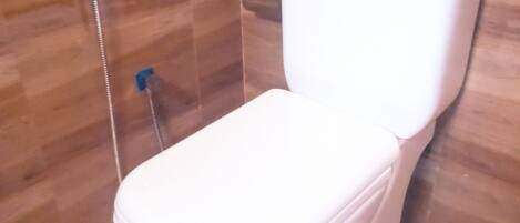 Un inodoro blanco en un baño con pared de azulejos y zona de ducha.