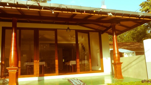 A covered outdoor area with a glass door leading to a room, a small garden, and a pathway. - Talalla Sea Anemone Hotel (Talalla)