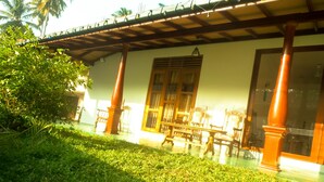 A covered outdoor area with a wooden bench and chairs, a large window, and a door. - Talalla Sea Anemone Hotel (Talalla)